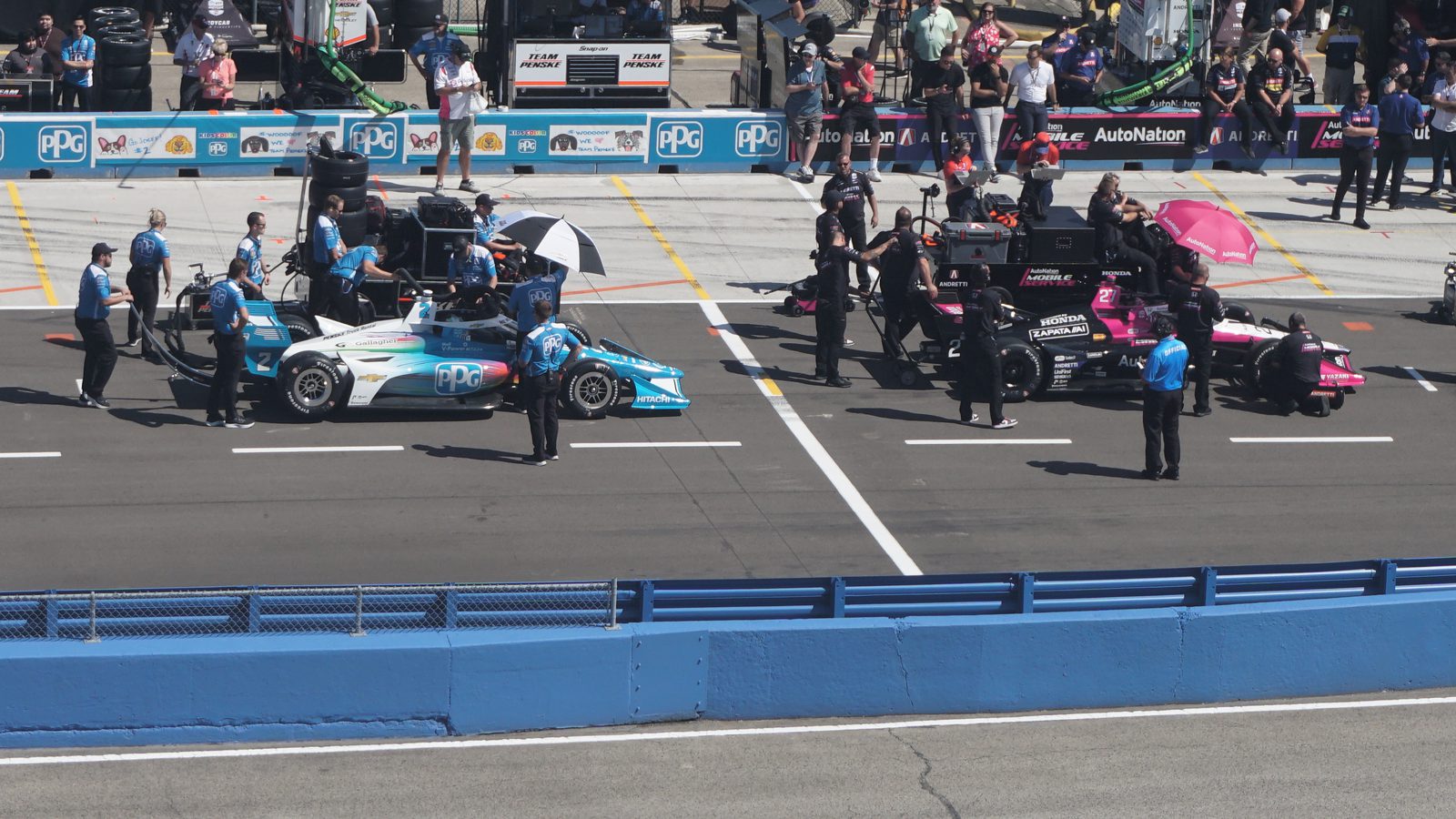 IndyCar Series cars on the starting grid with their crews
